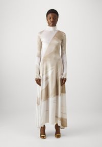 Langsleeve, figuurvolgend jurkje van zachte, rekbare stof met een beige en witte abstracte patroon, met een hoge kraag en een uitlopende zoom.