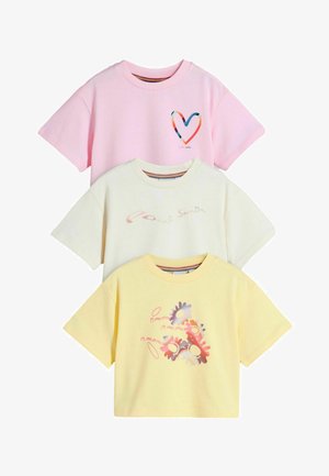 Kolme lyhythihaista t-paitaa pinossa: pinkki, jossa värikäs sydän, kerma, jossa hienovarainen teksti, ja keltainen, jossa pastellivärinen kukka- ja hammasrattukuvio.