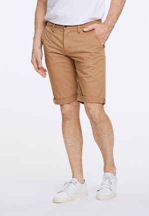 Khaki-Shorts mit umgeschlagenen Säumen, aus einem weichen Stoff gefertigt. Kombiniert mit weißen Sneakern für einen lässigen Look.