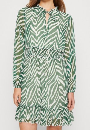 Green and white zebra-patterned dress with long sleeves, a tie neck, smocked waist, and ruffled hem. Made from lightweight, sheer fabric.