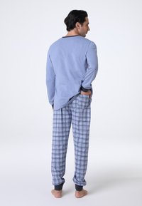 Maglia a maniche lunghe blu chiaro con colletto scuro, abbinata a pantaloni a quadri blu con vestibilità rilassata e polsini a coste alle caviglie.