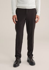 Crne krojene hlače s glatkom teksturom, slim fit krojem i suptilnim naborima. Uparene s tamnim čipkastim cipelama. Svijetla pozadina.