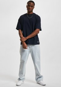 Marineblå t-skjorte med kort erm i avslappet passform, kombinert med lyseblå, løse jeans og hvite joggesko. Enkelt design med en subtil merkeetikett.