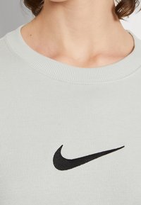 Ljusgrå sweatshirt med randig halsringning och muddar. Har en framträdande svart broderad Nike-logotyp framtill.