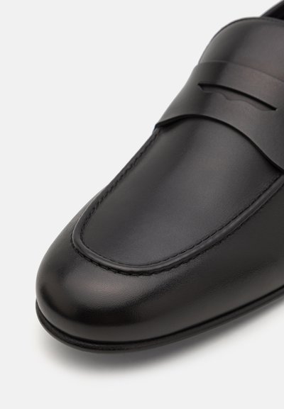 Mustad nahast loafers, millel on sile viimistlus, oktavad õmbluse ääres ja peene dekoratiivse riba ees.