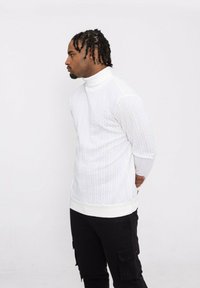 Pull en col roulé blanc texturé avec un motif côtelé, coupe ajustée et ourlet côtelé contrasté. Associé à un pantalon cargo noir.