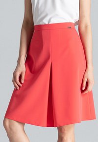 Koraalkleurige knielange rok met een gladde textuur, voorzien van een voorste plooi, hoge taille en een metalen merkaccent op de tailleband.