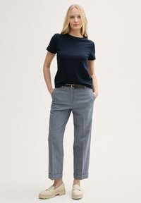 Top corto blu navy a maniche corte abbinato a pantaloni a quadri grigi. I pantaloni presentano un orlo a risvolto e un tessuto liscio. Le scarpe beige slip-on completano l'outfit.