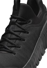 Černá sportovní bota s texturovaným textilním svrškem, plochými tkaničkami, výraznou gumovou podrážkou a minimalistickým designem. Značení na patě.