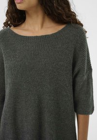Pulover verde din tricot cu textură zimțată, decolteu larg și mâneci până la cot. Țesătură moale cu o croială lejeră și relaxată.