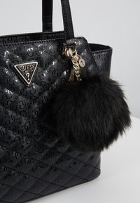 Sac à main synthétique noir avec motif en relief, ferrures dorées et pompon amovible en fourrure noire. Présente un logo triangulaire à l'avant.