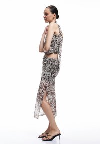 Leopardprint twee-delige outfit bestaande uit een aansluitende, gerimpelde crop top en een bijpassende rok met hoge split. Gemaakt van doorzichtig materiaal. Zwarte hakken.