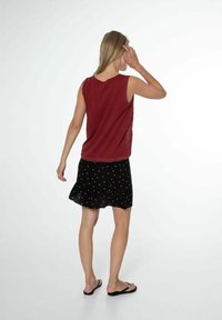 Top senza maniche color bordeaux, scollatura rotonda; abbinato a una gonna nera con punti metallici, orlo a volant e tessuto leggero.