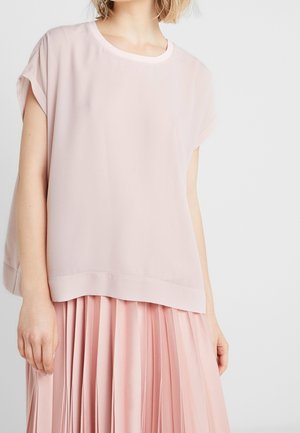 Top corto de manga corta en rosa claro, con escote redondo y corte relajado. Combinado con una falda plisada del mismo tono para un look coordinado.