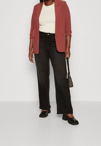 Lätt, figurnära rödbrun blazer, ribbad krämfärgad topp, hög midja svarta vida jeans och kraftiga svarta klackar. Svart handväska med mönstrade detaljer.