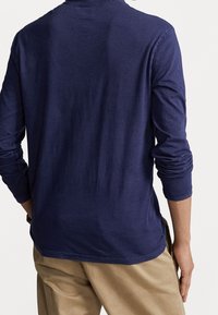 Marinblå långärmad T-shirt med rund halsringning och en avslappnad passform, med mjuk textur och lätt rynkning vid ärmarna. Invikt i beige byxor.