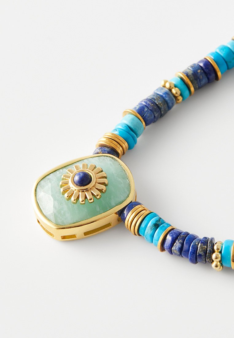 Türkiser und blauer Perlenhalskette mit einem rechteckigen grünen Stein in der Mitte, verziert mit einem goldenen Sonnenstrahlenakzent und goldenen Ringen.