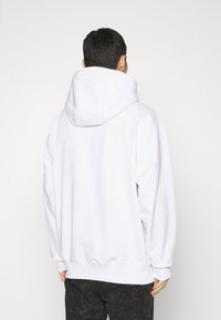 Weißer Kapuzenpullover mit lockerer Passform, ausgestattet mit einer großen Kapuze und gerippten Bündchen. Glatte Stoffoberfläche ohne erkennbare Muster.
