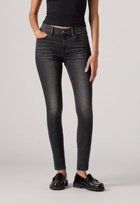 Jeans skinny neri in denim, con un classico design a cinque tasche, leggermente sbiaditi e abbinati a mocassini neri.