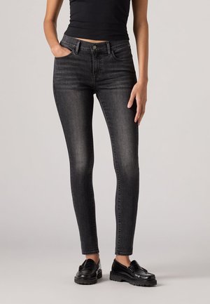 Schwarze, enge Jeans aus Denim mit klassischem Fünf-Taschen-Design, dezenten Verblassungen und kombiniert mit schwarzen Slippern.