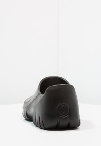 Schwarzer Slipper aus Gummi mit glatter Textur, runder Form und dicker Sohle, die ein dezentes geprägtes Logo-Detail aufweist.