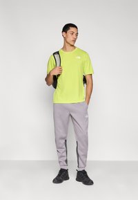 Λαχανί κοντομάνικο T-shirt, γκρι φόρμα με πλαϊνές λωρίδες και μαύρα αθλητικά παπούτσια. Απλός σχεδιασμός, άνετο ύφασμα.