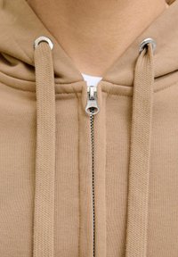 Brązowy hoodie na zamek wykonany z miękkiej mieszanki bawełny, z metalowym zamkiem błyskawicznym, teksturowanymi sznurkami oraz żeberkowymi akcentami wokół dekoltu.