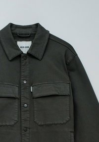 Donkergrijze denimjacket met een spitse kraag, voorzijde met drukknoopjes en twee borstzakken met kleppen. Lichtgewicht stof.