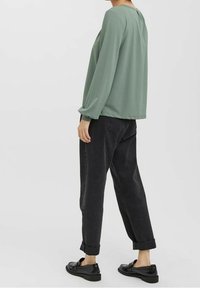 Blouse verte à manches longues avec un col rond, associée à un jean noir fuselé, retroussé aux chevilles, et des chaussures plates noires.