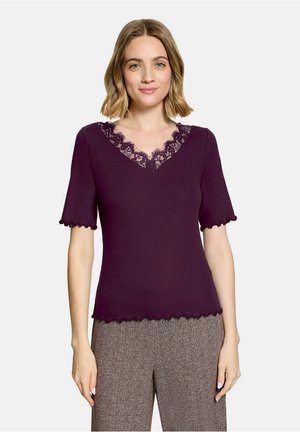 Woman wearing a purple short-sleeve top with lace trim at the V-neck and edges, paired with brown patterned wide-leg pants.