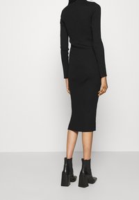 Schwarzes, geripptes Strickkleid mit langen Ärmeln, figurbetonte Silhouette, knielange Länge, getragen zu schwarzen Blockabsatz-Stiefeletten.