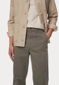 Helles beige Knopfjackett mit aufgesetzten Taschen, getragen über einem cremefarbenen Hemd, kombiniert mit olivgrünen Hosen mit geradem Schnitt.
