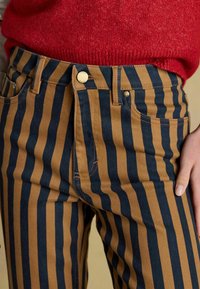 Pantaloni din bumbac cu dungi verticale bleumarin și cămilă, închidere cu nasture metalic și design cu cinci buzunare. Textură moale cu cusături vizibile.