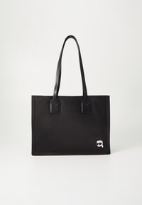 Czarna prostokątna torba na ramię z podwójnymi cienkimi uchwytami i małą naszywką z rysunkową twarzą w okularach przeciwsłonecznych w prawym dolnym rogu.