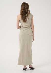 Beige sleeveless top and long skirt with an asymmetrical hemline. Soft fabric with a slight sheen, paired with black open-toe heels.