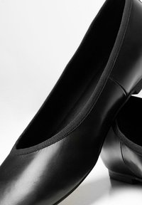 Bailarinas de cuero negro con un acabado suave, bordes elásticos y un tacón bajo, que presentan un diseño de punta redonda.