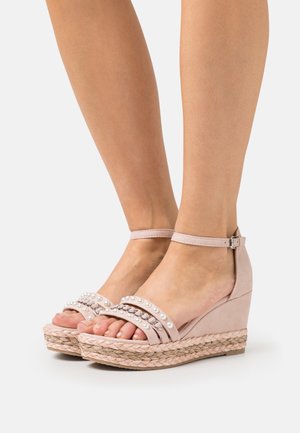 Sandalias de cuña beiges con parte superior de tela texturizada, dos correas anchas adornadas con pequeñas perlas y una suela de plataforma envuelta en yute.