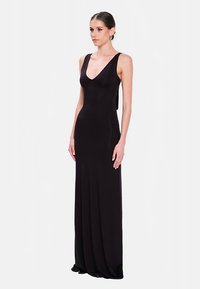 Robe noire sans manches, longue jusqu'au sol, avec un décolleté en V profond et une silhouette ajustée ; fabriquée dans un tissu lisse et extensible, mettant en valeur les contours.