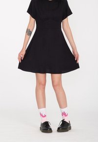 Vestito nero a maniche corte con corpetto aderente e gonna svasata. Indossato con calzini bianchi con motivi di fiamme rosa e scarpe nere.