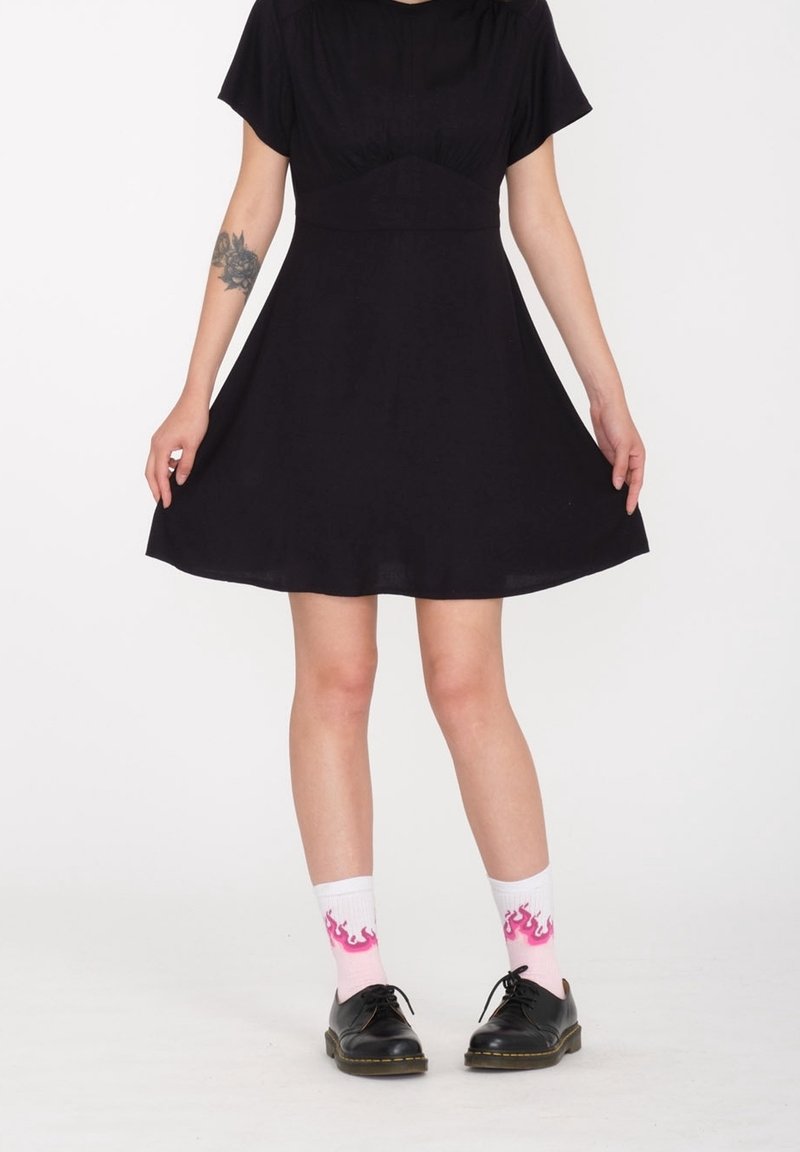 Vestito nero a maniche corte con corpetto aderente e gonna svasata. Indossato con calzini bianchi con motivi di fiamme rosa e scarpe nere.
