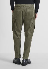 Pantalones cargo de pana en verde oliva con cinturilla elástica, dos bolsillos traseros y dos bolsillos laterales. Tejido texturizado con un diseño de pierna ajustada.