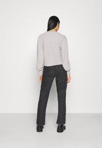 Světle šedý, zkrácený svetr s nabíranými rukávy, kombinovaný s tmavými džíny. Svetr má kulatý výstřih a žebrované manžety.