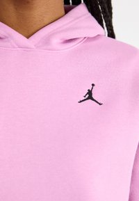 Pink hoodie with a prominent black Jordan logo on the chest. The fabric is soft and textured, featuring a classic hood design.