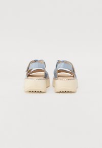 Sandales à plateforme avec des brides synthétiques bleues, semelles beiges et détails tissés. Design à dos ouvert avec des brides ajustables pour un bon maintien.