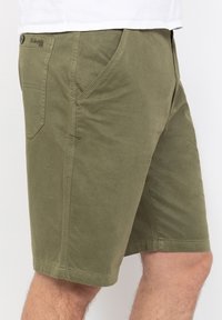 Pantalones cortos verde oliva hechos de un suave tejido de algodón, con bolsillos laterales, un bolsillo trasero tipo parche y un dobladillo cosido. Cierre de botón en la cintura.