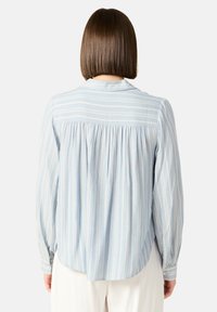 Camicia a maniche lunghe blu chiaro con righe verticali bianche, caratterizzata da un retro plissettato e polsini con bottoni, realizzata in tessuto morbido.
