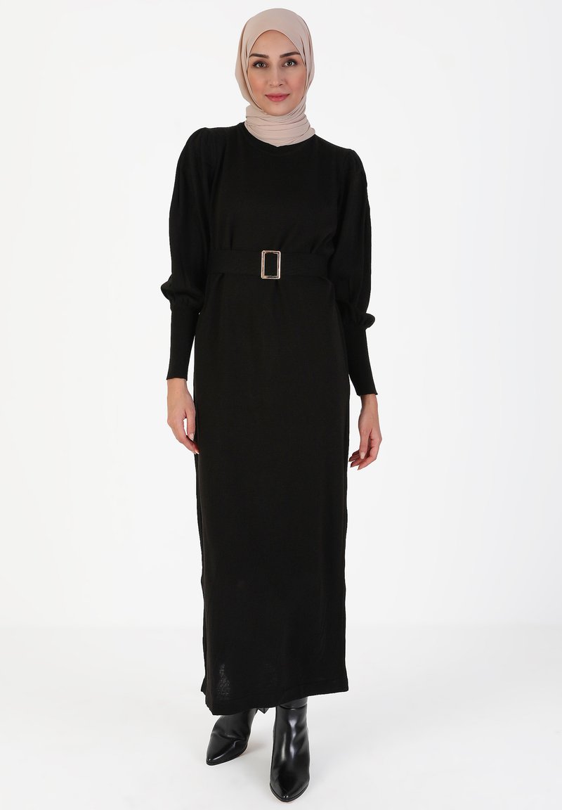 Vestito nero a maniche lunghe con vita cinturata, caratterizzato da un colletto rotondo e un tessuto testurizzato. Abbinato a eleganti stivaletti neri alla caviglia.