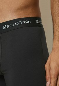 Schwarze Baumwoll-Boxershorts mit einem weichen Bund, der das weiße Logo "Marc O'Polo" zeigt. Nahaufnahme, die die Stofftextur und den Sitz betont.