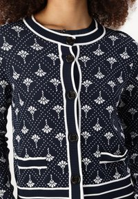 Navy cardigan featuring a white floral pattern, ribbed collar, and cuffs, with two front pockets and dark buttons.