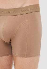 Nahaufnahme von hellbraunen Herren-Boxershorts mit sichtbaren Nähten und einem elastischen Bund mit dem Markennamen.